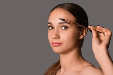 Gri arka planda kaşlarını düzelten genç bir kadın.
