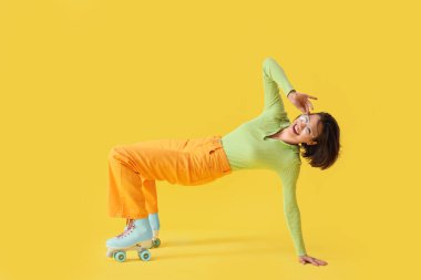 Sarı arka planda poz veren patenli mutlu genç kadın.