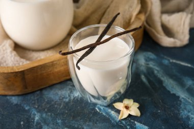 Bir bardak taze vanilyalı süt ve mavi arka planda çiçek.