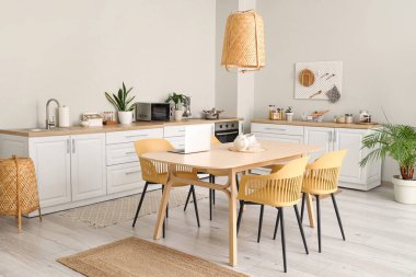 Modern mutfak, beyaz tezgahlar, yemek masası, dizüstü bilgisayar, sandalyeler ve lamba.