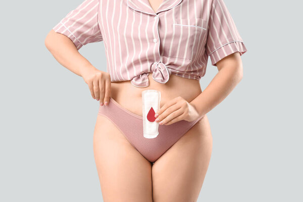 Молодая женщина в период трусики держа площадку с бумажной каплей крови на белом фоне