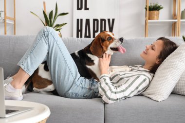 Evdeki kanepede tatlı Beagle köpeği olan genç bir kadın yatıyor.