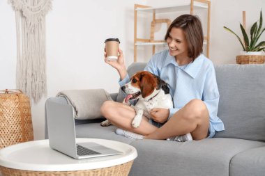Evdeki kanepede oturan bir fincan kahve ve sevimli bir tazı köpeğiyle genç bir kadın.