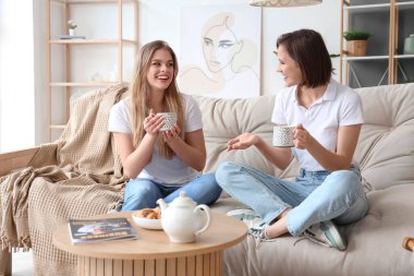 Bayan arkadaşlar evdeki kanepede çay içiyorlar.