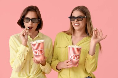 Pembe arka planda patlamış mısırlı 3 boyutlu gözlüklü bayan arkadaşlar.