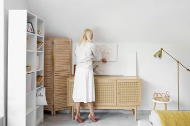 Olgun bir kadın evdeki ışık duvarına güzel bir resim asıyor.