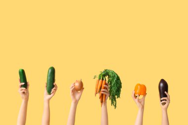 Female hands holding fresh vegetables on yellow background