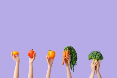 Female hands holding fresh vegetables on lilac background