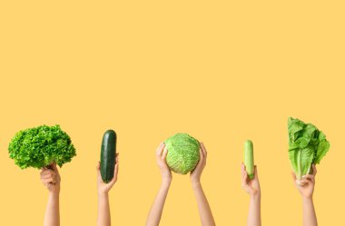 Female hands holding fresh vegetables on yellow background