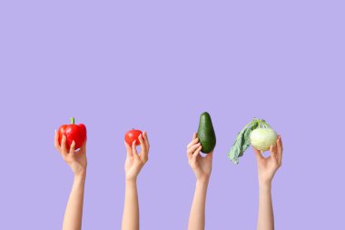 Female hands holding fresh vegetables on lilac background