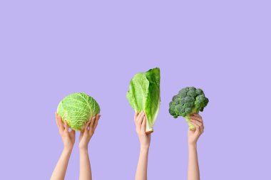 Female hands holding fresh vegetables on lilac background