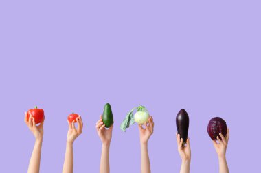 Female hands holding fresh vegetables on lilac background