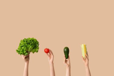 Female hands holding fresh vegetables on beige background