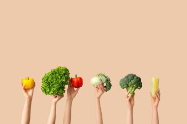 Female hands holding fresh vegetables on beige background