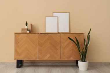 Boş çerçeveli ahşap dolap, bej duvarın yanında kitaplar ve bitkiler.