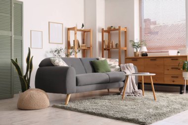 Modern oturma odasının içinde gri kanepe, kahve masası ve beyaz duvarda boş çerçeveler.