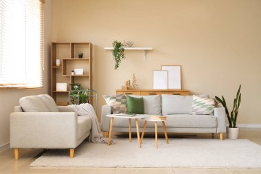 Modern oturma odasının içinde gri kanepeler, sehpa ve ahşap dolapta boş çerçeveler var.