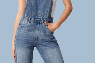 Şık bir kot pantolon giymiş, mavi arka planda güzel bir genç kadın.