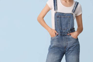 Şık bir kot pantolon giymiş, mavi arka planda güzel bir genç kadın.