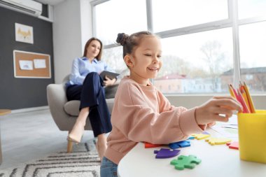 Psikologun ofisinde çizim yapmak için kalem alan küçük kız.