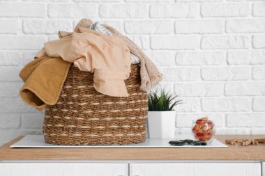 Çamaşır odasındaki sepetin üstünde çamaşır deterjanı ve kapsülleri var.