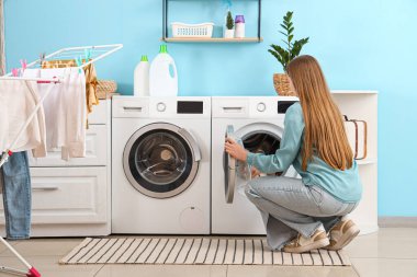 Çamaşır odasında çamaşır makinesine çamaşır koyan bir kadın.