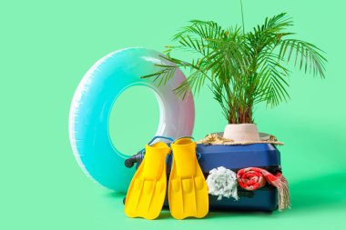 Şık plaj aksesuarları, şişirilebilir yüzük ve yeşil arka planda egzotik bitki dolu bavul.