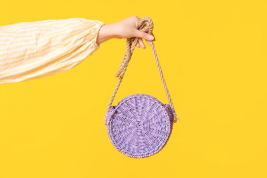 Sarı arka planda zarif mor hasır çantalı bir kadın.