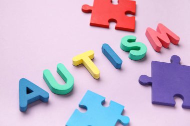 Kelime AUTISM ve eflatun arkaplan üzerindeki renkli yapboz parçaları