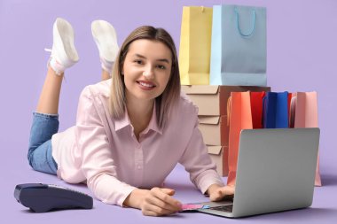 Diz üstü bilgisayarı olan genç bir kadın leylak arka planda alışveriş yapıyor.