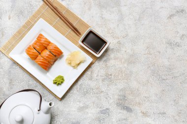 Soya soslu lezzetli suşi ruloları, yemek çubukları ve gri grunge arka planda çaydanlık.