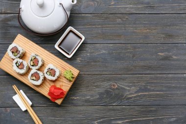 Soya soslu lezzetli suşi ruloları, yemek çubukları ve ahşap zemin üzerinde çaydanlık.