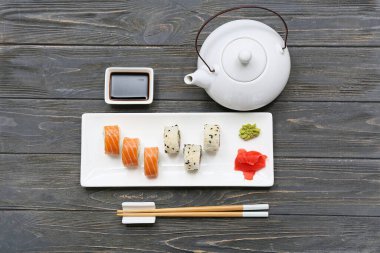 Soya soslu lezzetli suşi ruloları, yemek çubukları ve ahşap zemin üzerinde çaydanlık.
