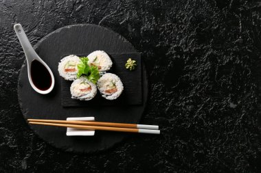 Lezzetli suşi ruloları ve çubuklar, siyah grunge arkaplanda soya soslu kaşık.