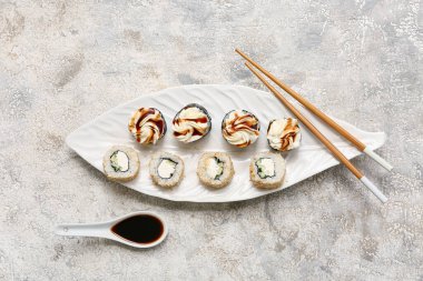 Gri grunge arka planda lezzetli suşi ruloları, yemek çubukları ve soya soslu tabak.