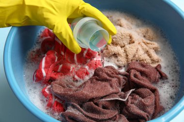 Plastik eldivenli kadın plastik leğende çamaşırlara deterjan ekliyor.