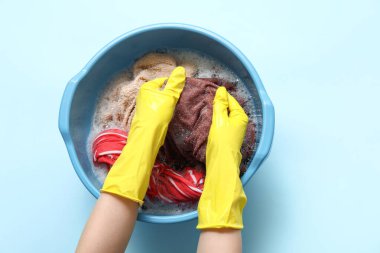 Lastik eldivenli bir kadın mavi arka planda plastik bir leğende çamaşır yıkıyor.