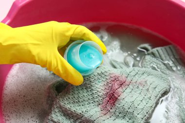 Plastik eldivenli kadın plastik leğende çamaşırlara deterjan ekliyor.