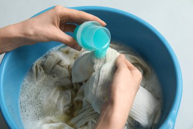 Gri arka plandaki plastik havuza çamaşır deterjanı ekleyen kadın, yakın plan.