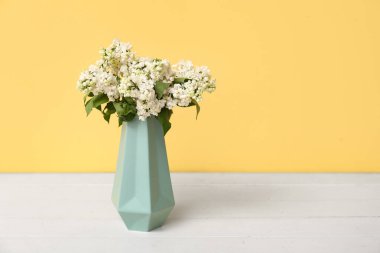 Sarı arka planda, beyaz ahşap masada çiçek açan güzel leylak vazosu.
