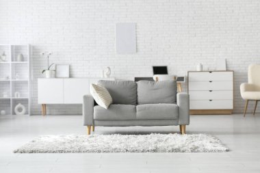 Aydınlık oturma odasının içinde gri kanepe, çekmece ve halı var.