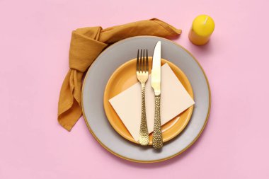 Altın çatal bıçak takımı ve pembe arka planda mum olan güzel bir masa.