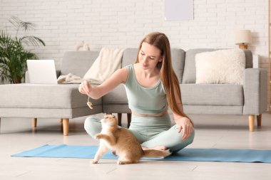 Evde yoga minderinde kedi yavrusuyla oynayan genç bir kadın.