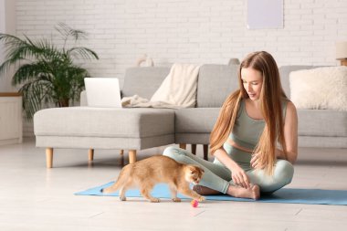 Evde yoga minderinde kedi yavrusuyla oynayan genç bir kadın.