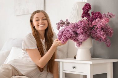 Genç bir kadın vazonun yanında yatıyordu. Evde komodinin üzerinde leylaklar vardı.