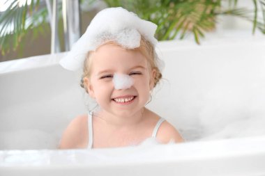 Küçük tatlı kız banyoda köpükle banyo yapıyor.