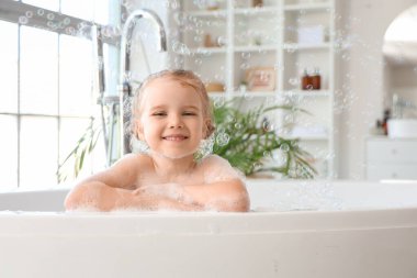 Tatlı küçük kız köpükle banyo yapıyor ve sabun köpüğü banyoda banyo yapıyor.