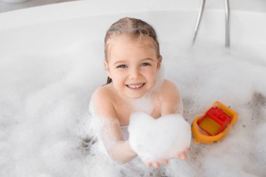 Oyuncak ve köpüklü şirin küçük kız banyoda banyo yapıyor.