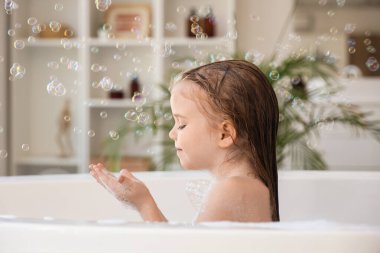 Sabun köpüklü şirin küçük kız banyoda banyo yapıyor.