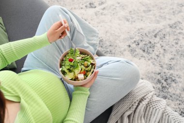 Taze sebze salatalı hamile kadın evdeki kanepede oturuyor.